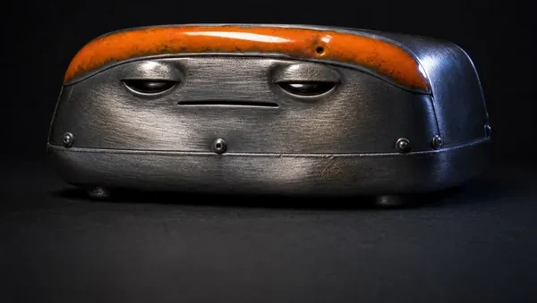 SLAB, a gunmetal and fired orange enamel creature, photographed as a specimen on a dark ground.